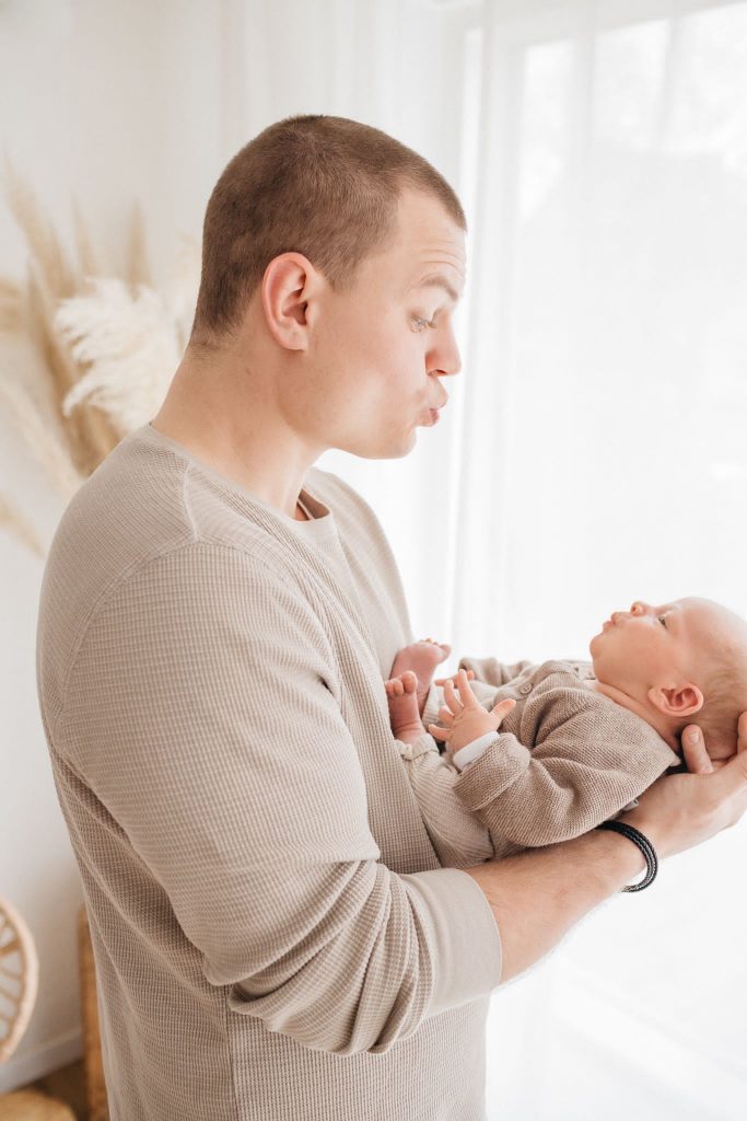 Babyshooting, Newbornshooting, Geschwisterbilder bei vavrova-photography Papa hält Baby mit Kussmund Newborn-Idee